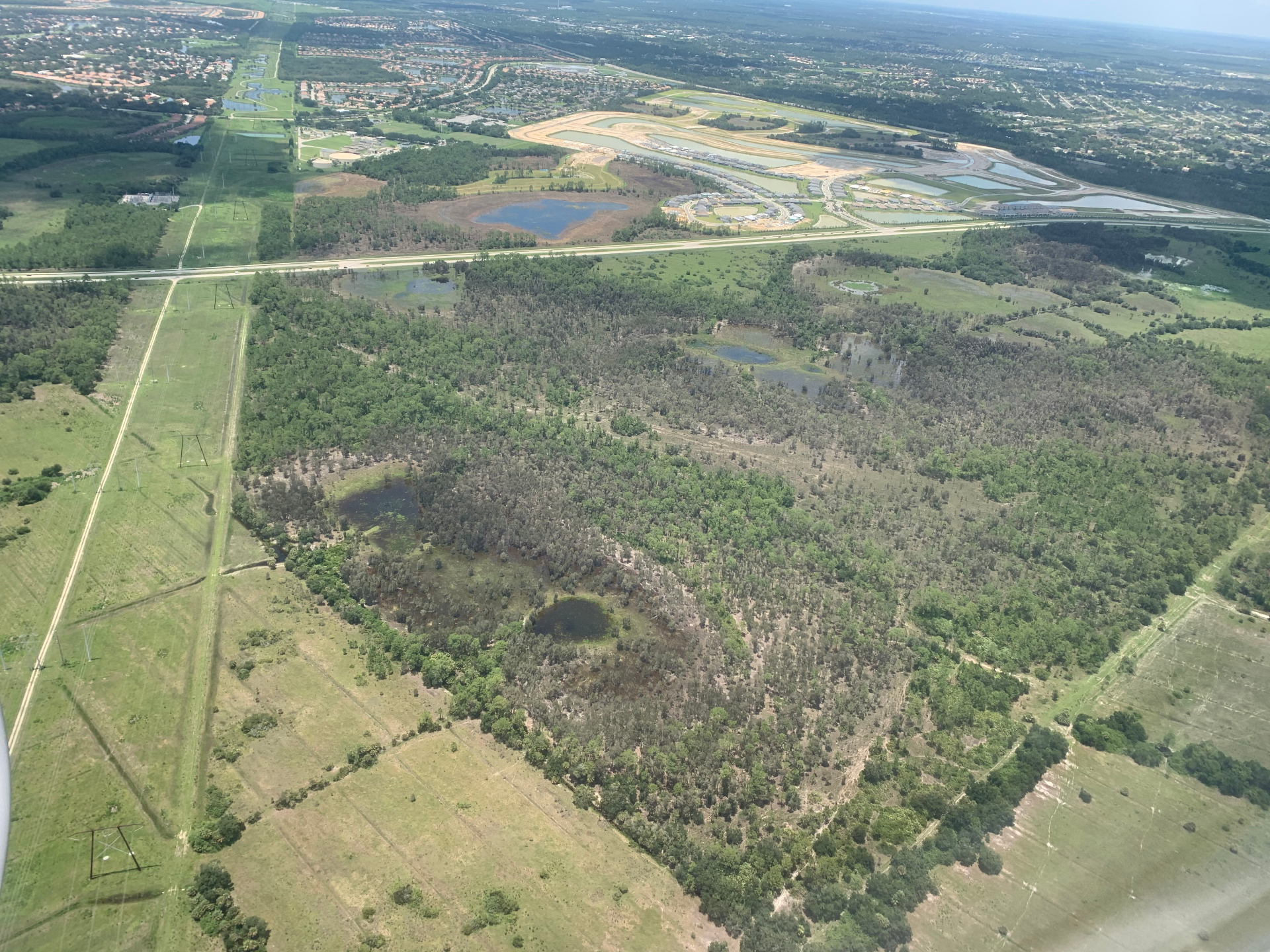 Aerial view of a Florida forested wetland complex bordered by highway, transmission corridor, and suburban development.